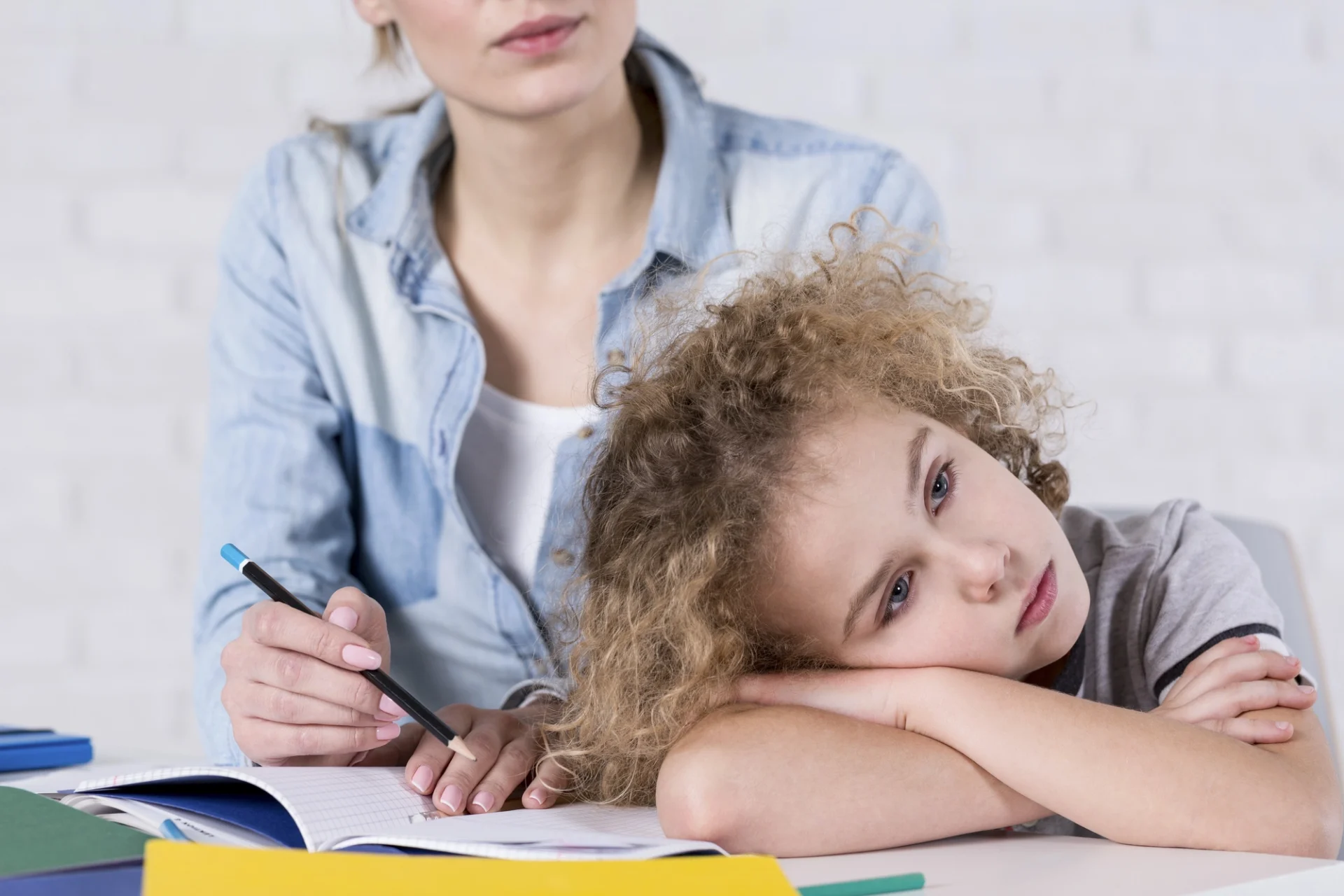sad looking child with his head on a table in front of a teacher or tutor