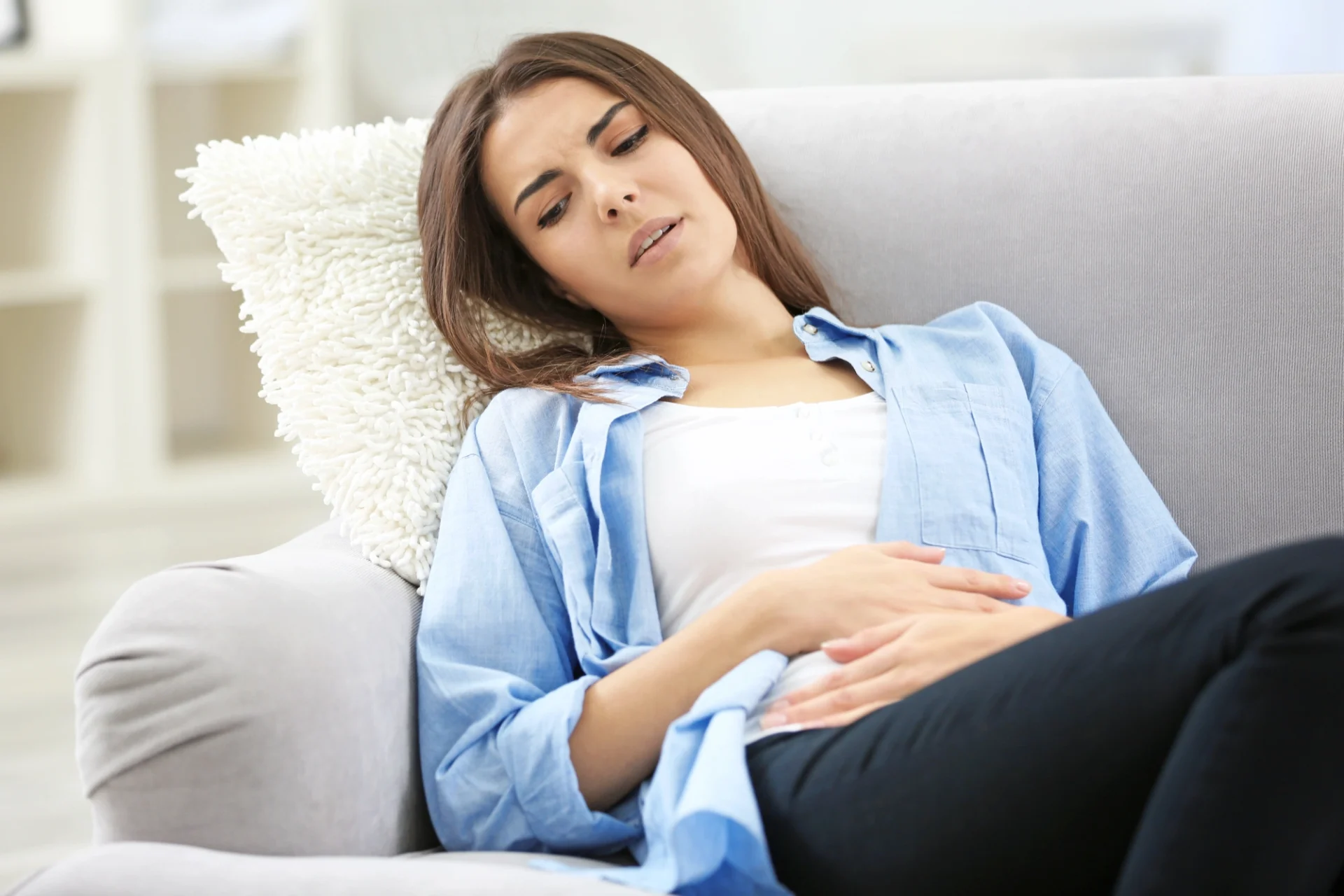 young woman leaning back into a couch cushion with hands over her abdomen
