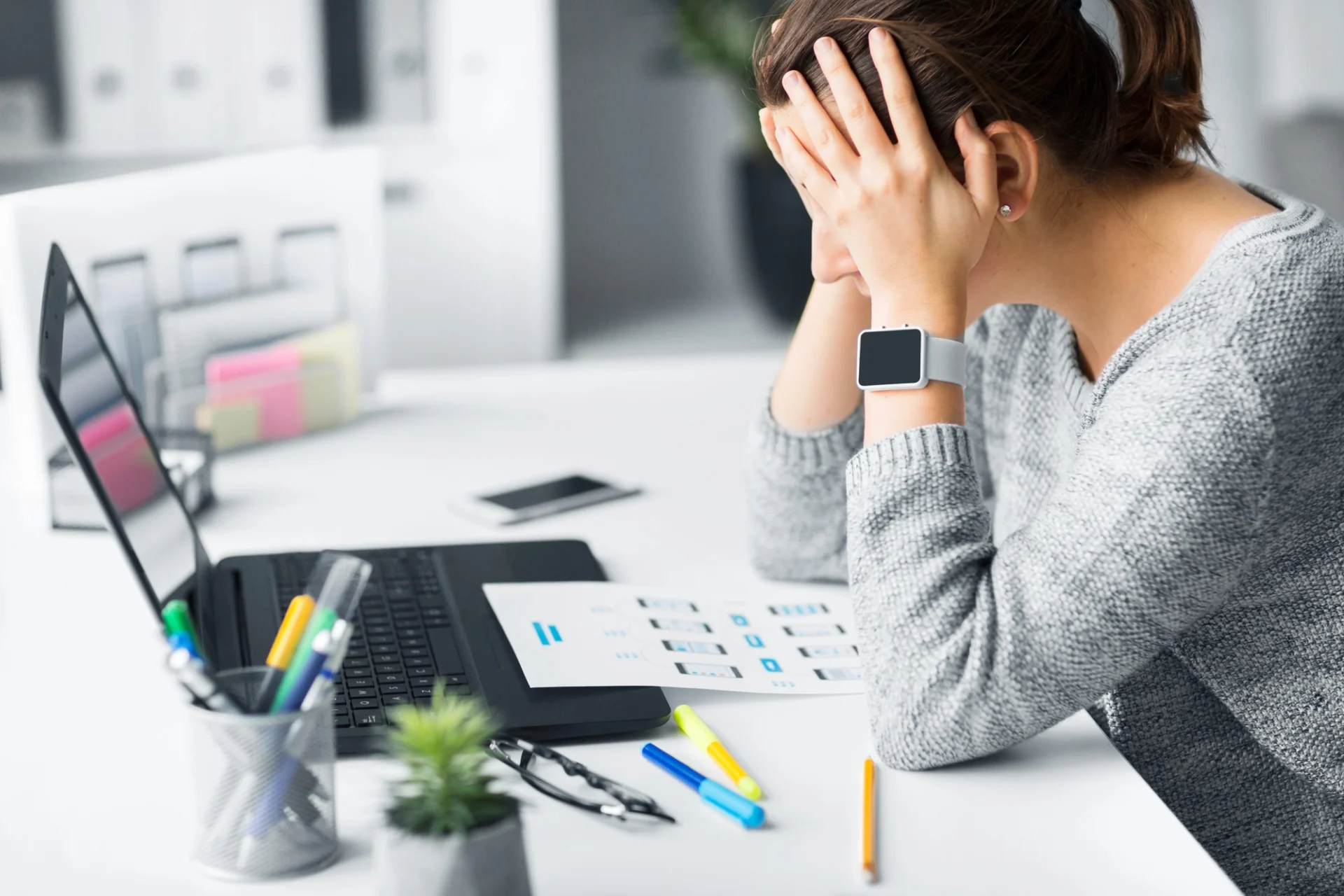 stressed woman hunched over laptop holding her head in her hands