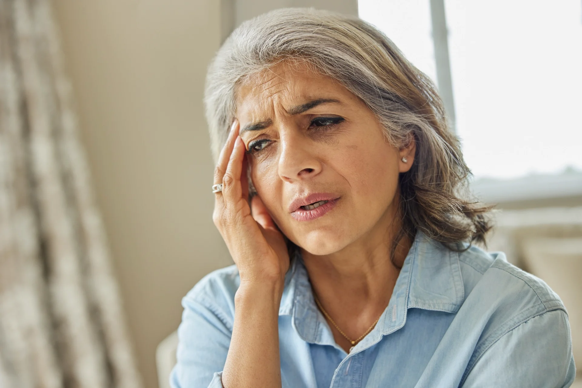 elderly woman with her hand near her eye and a confused look on her face