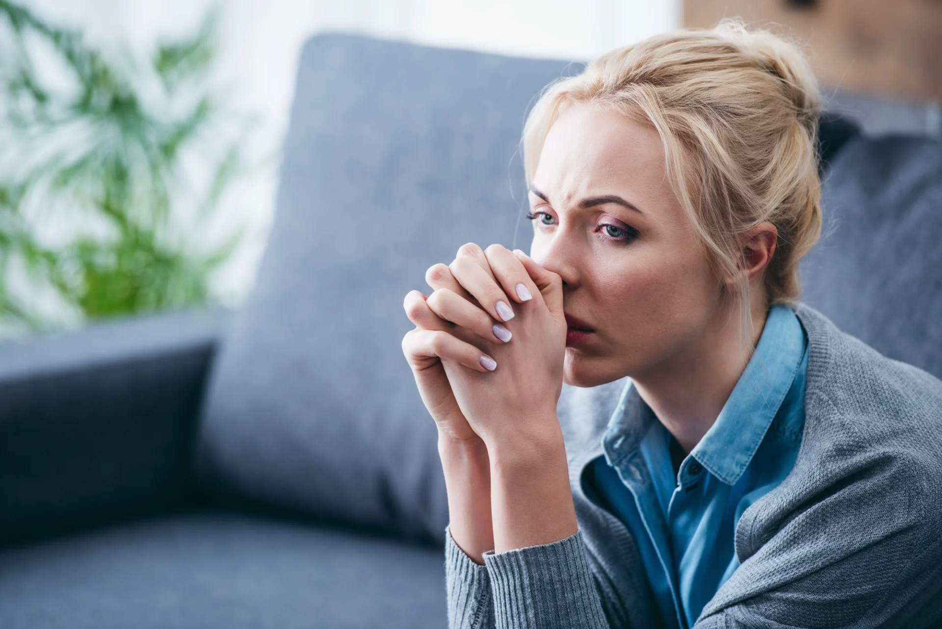 sad, pensive looking blonde woman with her hands clasped in front of her face