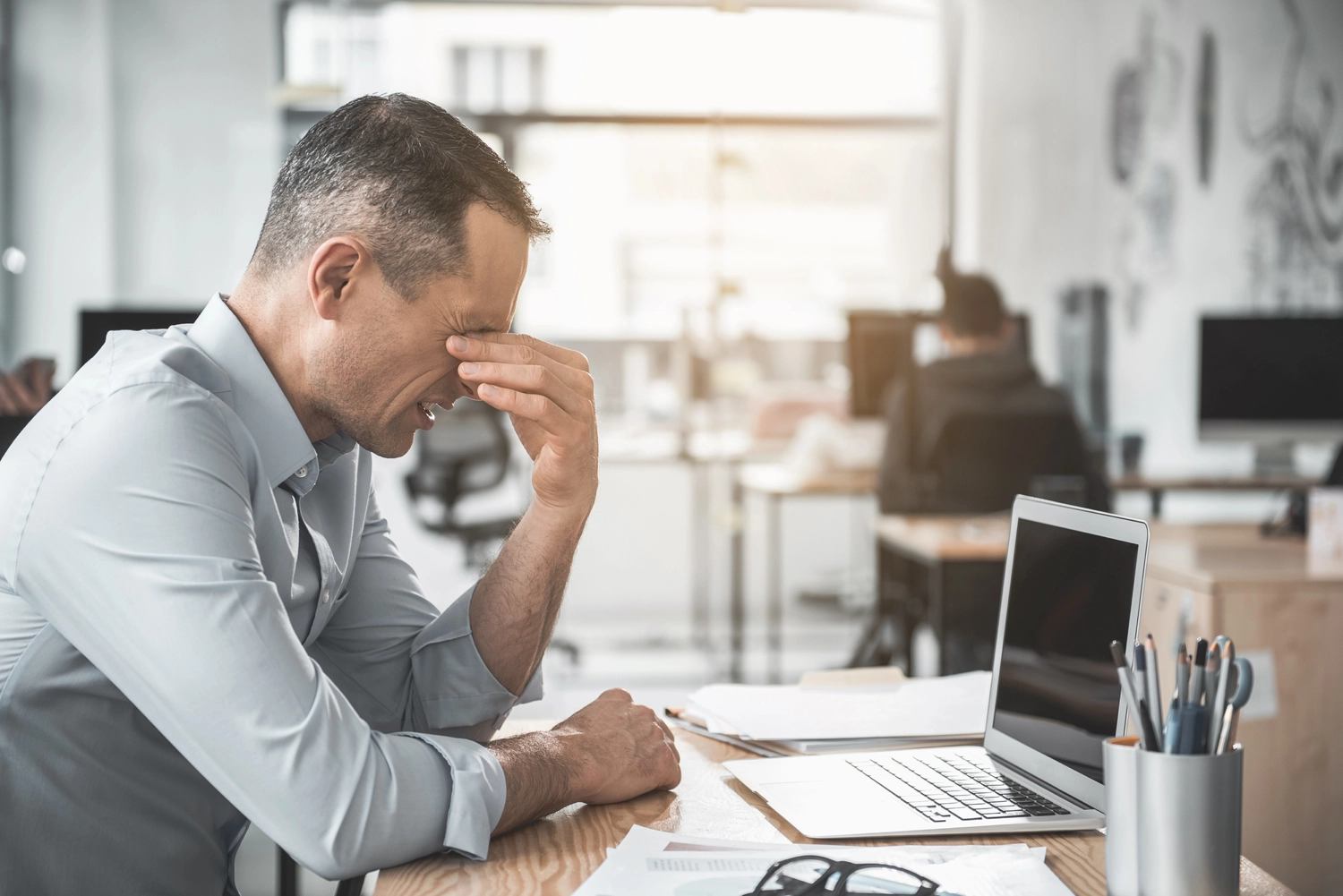 man sitting behind laptop looking anxious and stressed while pinching his sinuses