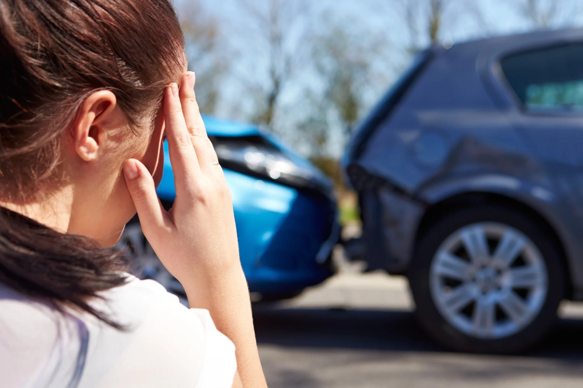 close up of a woman touching her forehead with a car accident in the background
